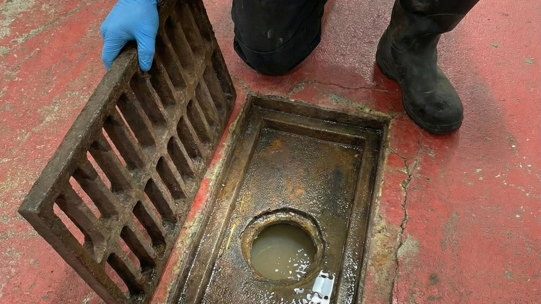 Dirty old cast iron grated area drain in food facility with cracked floors around it